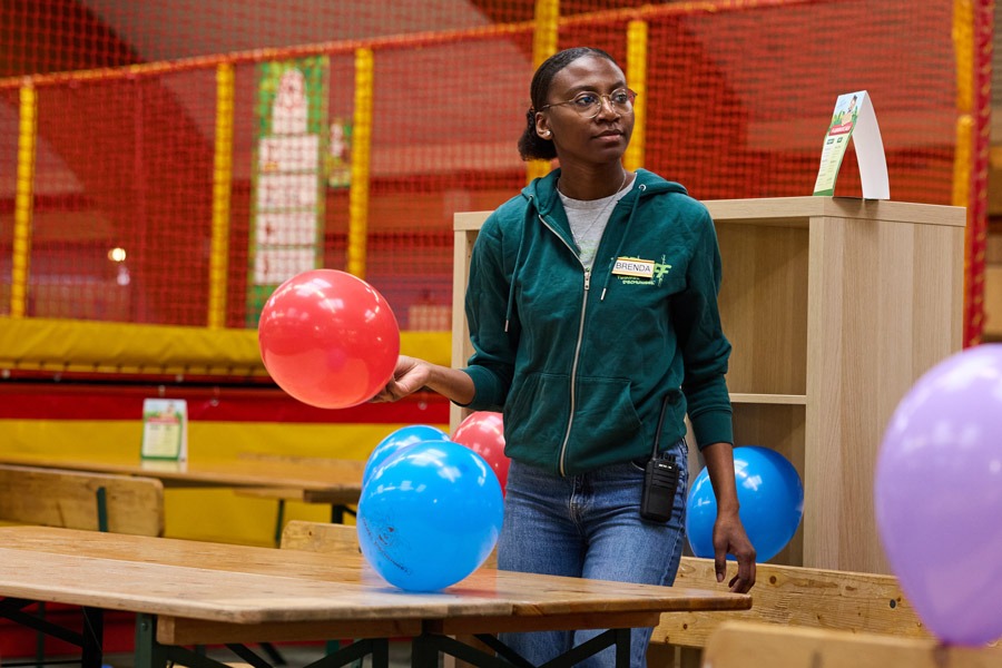Mitarbeiterin dekoriert im Indoorspielplatz Tische mit bunten Luftballons